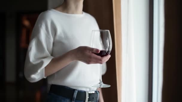 女の子はガラスからワインを飲み 窓の近くに立っている カメラはガラスを見て女の子の顔に向かって立ち上がり — ストック動画