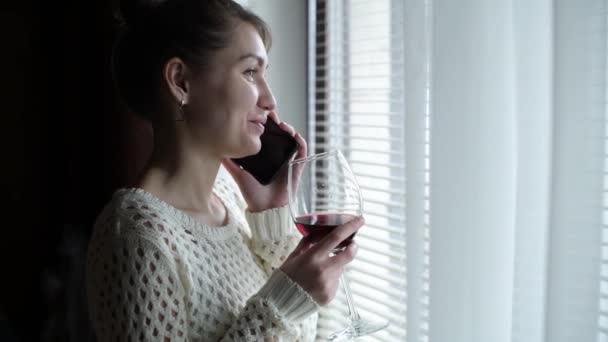 笑顔の女の子が窓の近くの電話で話しワインを飲み笑いカメラが動き — ストック動画