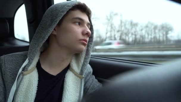 一个少年坐在汽车后座上 向窗外看去 然后被收到的电话分散了注意力 相机在微微摇晃 — 图库视频影像