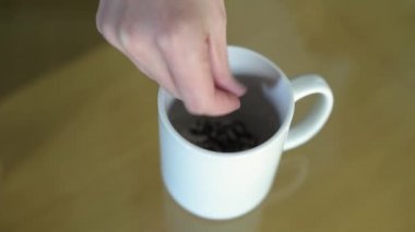 Kız fincana çay yaprakları döküyor ve kaynar su döküyor. Kupada çay demlemek. Kapat, üst görünüm