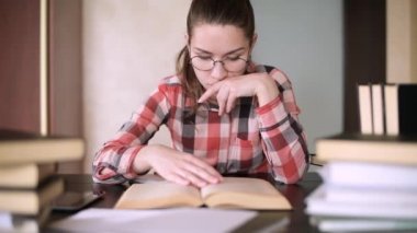Gözlüklü kız eğitimle meşgul, kitaplarla dolu bir masada oturuyor. Sınav Hazırlık Seansı. Mesafe, karşılıklı eğitim. Karantina ve kendini izole etme