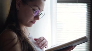 Kız kitap okuyor ve çay ya da kahve içiyor, yakın plan, yan görüş.