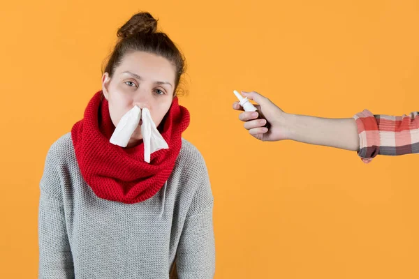 A girl with a cold and a runny nose is offered a spray for the nose. The girl s nostrils are stuffed with napkins, the hand holds out a vasoconstrictor