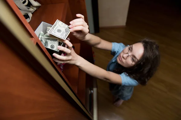 Bir Kız Dolabın Üst Rafındaki Bir Para Kutusundan Dolar Alır — Stok fotoğraf