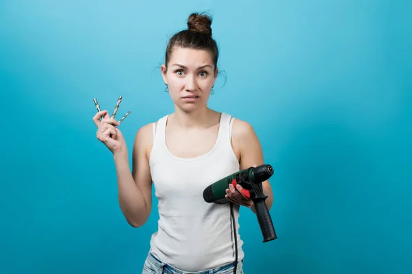 Portrait of a girl who does not understand how to use a drill. A male tool in the hands of a misunderstood girl