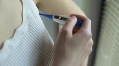 Kız elektronik termometreyi açıyor ve koltukaltına yerleştiriyor. Vücut ısısı ölçümü. Kapat.