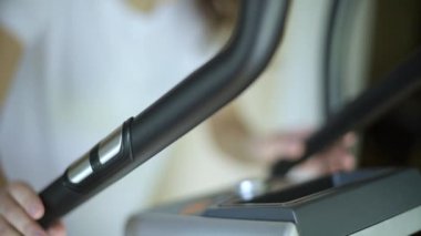 Kız elipsoid üzerinde yapılan kardiyo çalışmasında kalp atış sensörü tutuyor. Yaklaş, seçici odaklanma. Evde spor ve spor