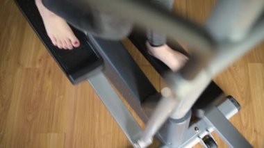 Bir kadın bir elipsoid üzerinde eğitime başlar ve biter. Pedalların üstündeki bacakların üst görüntüsü. Evde spor ve spor