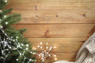 Ahşap bir masa üzerinde ladin dalları. Tahtanın üstündeki Noel süsleri yukarıdan görülüyor. Reklam ürünleri, dekorasyonlar ve metin için yer.