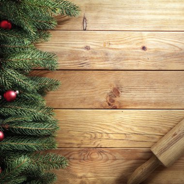 Ahşap bir masa üzerinde ladin dalları. Tahtanın üstündeki Noel süsleri yukarıdan görülüyor. Reklam ürünleri, dekorasyonlar ve metin için yer.