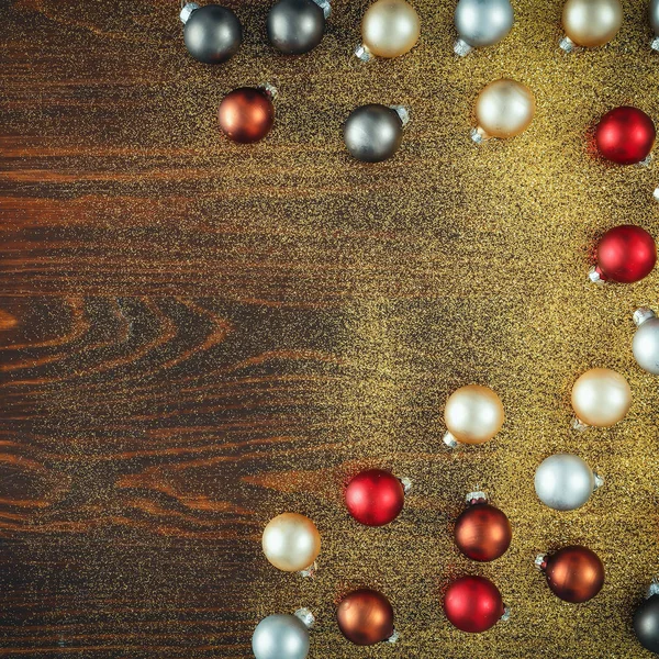 Shiny glowing small baubles on a flat wooden background. Glimmering, shimmering winter christmas background. Space for advertising products, decorations and text.