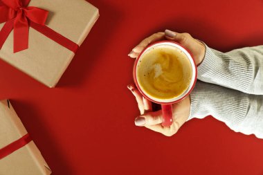 Kadının ellerinin sıcak içeceğe dokunuşunun üst görüntüsü. Dekorasyonun için bedava yer. Bir fincan sıcak çikolata ya da kahve. Masanın üstü kırmızı. Noel zamanı. Uzayı kopyala, havadan bak. Gölgeli karanlık ruh hali aydınlığı