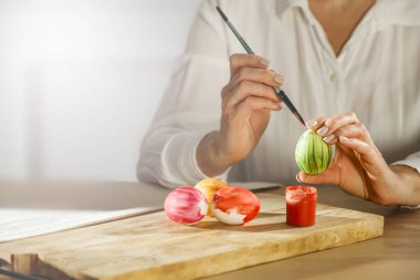 Bir bahar günü tahta masaya paskalya yumurtası boyayan kadın eller. Paskalya süsü zamanı. Tahtaya renkli yumurta ve boya..