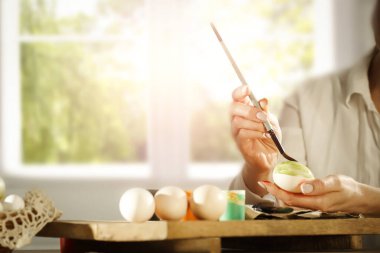 Bir bahar günü tahta masaya paskalya yumurtası boyayan kadın eller. Paskalya süsü zamanı. Tahtaya renkli yumurta ve boya..