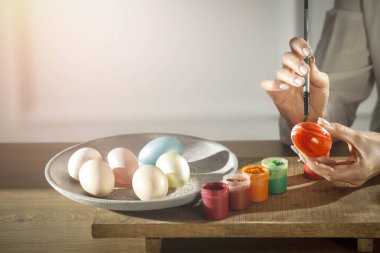 Bir bahar günü tahta masaya paskalya yumurtası boyayan kadın eller. Paskalya süsü zamanı. Tahtaya renkli yumurta ve boya..