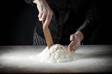 Mutfak masasındaki un sabah ışığında karamsar bir zemin üzerinde. Bir kadının elleri süzgeçten un geçiriyor..