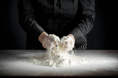 Mutfak masasındaki un sabah ışığında karamsar bir zemin üzerinde. Bir kadının elleri süzgeçten un geçiriyor..