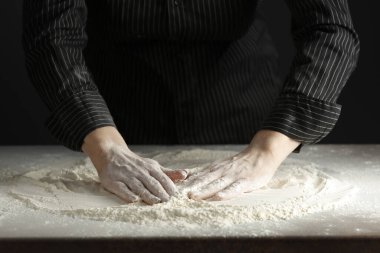 Mutfak masasındaki un sabah ışığında karamsar bir zemin üzerinde. Bir kadının elleri süzgeçten un geçiriyor..