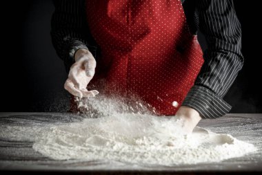 Mutfak masasındaki un sabah ışığında karamsar bir zemin üzerinde. Bir kadının elleri süzgeçten un geçiriyor..