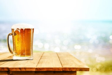 Büyük bardakta soğuk bira, ahşap masada, okyanus ve kumlu plaj arka planında. Reklam ürünleri için alanı kopyala.