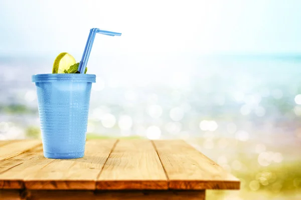 Cold drink on wooden table with ocean and sandy beach background. Copy space for advertising product. Beautiful sunny summer time and relaxation.