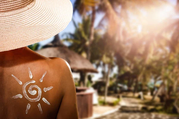 Woman in a sun straw hat with sun cream on her back and blurred sunlight summer background. Copy space for your decoration.