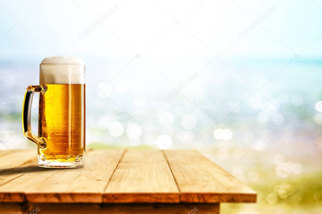 Cold beer in big glass on wooden table with ocean and sandy beach background. Copy space for advertising product.