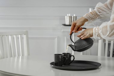 Zarif bluzlu kadın elleri beyaz masada fincanlara çay döküyor..