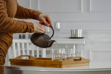 Kadın elleri çaydanlıktan bardaklara kahve dolduruyor. Beyaz ev içi arka plan.