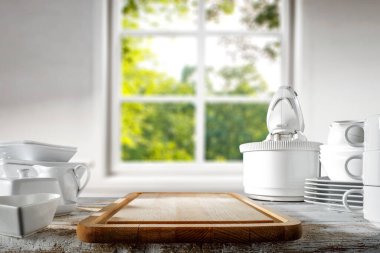 Karıştırıcı, mutfak gereçleri, tabaklar, aşınmış eski ahşap mutfak masası ve beyaz ışıklı mutfak penceresinin bulanık arka planı.