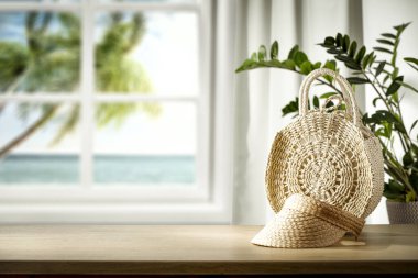 Beyaz pencere ve ahşap masa arkası hasır şapka, saman torbası ve pencerenin dışında mavi okyanus manzaralı..