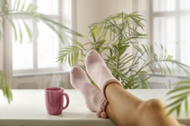 Bacaklar masanın üzerinde çoraplar ve bahar güneşi pencerenin dışında.