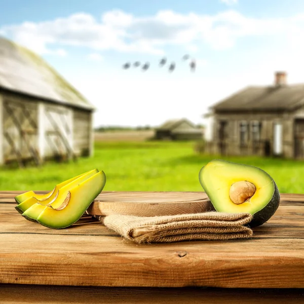 Fresh cut avocado, fruit cut in halves on wooden table top. Blurred cottage background. Sunny morning in the garden.