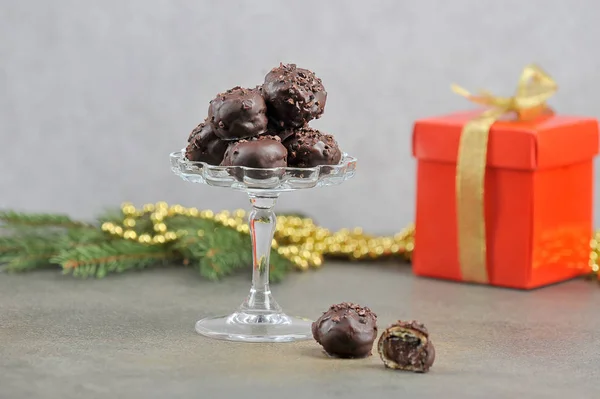 Handmade chocolate candies in a glass vase.  In the background is a gift box and a fir branch.  Gray background.