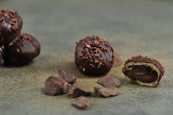 Handmade chocolates and pieces of dark chocolate on a dark surface.  One of the sweets is broken into two parts to demonstrate the filling.  Close-up.  Macro shot.