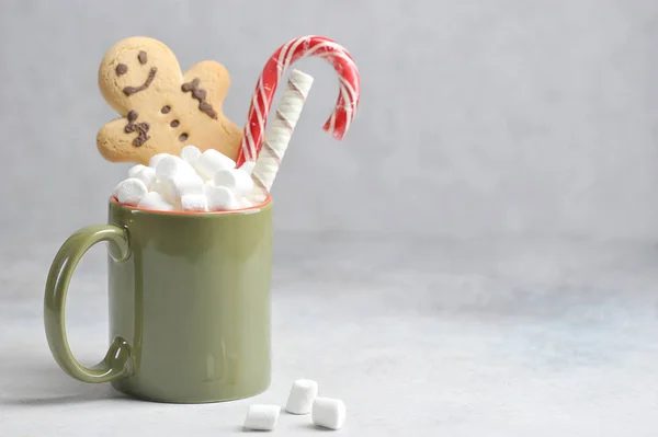 Hot drink with marshmallows. In a cup there is a gingerbread man, a candy Christmas cane and a waffle roll. Light background. Free space for text.