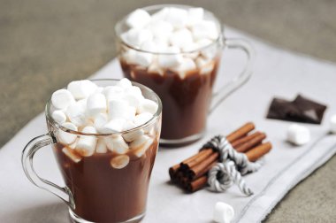 Şekerlemeli sıcak çikolata. İki fincan. Tarçın çubukları ve siyah çikolata parçaları kompozisyonu tamamlıyor. Yakın plan. Gri arkaplan.