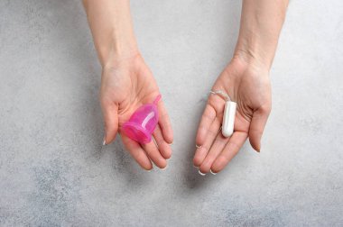 Adet bardağı ve kadın ellerinde klasik tampon. Kadın rahatlığıyla ilgilenme konusundaki seçim ve yenilik kavramı. Yakın plan. Yukarıdan bak. Hafif arkaplan.