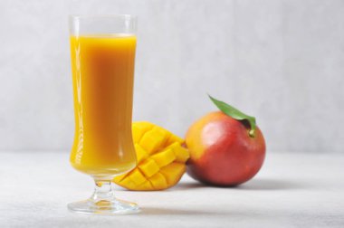  Uzun bardakta mango suyu. Bütün mango ve meyvelerin yarısı kompozisyonu tamamlıyor. Hafif arkaplan. Yakın plan..