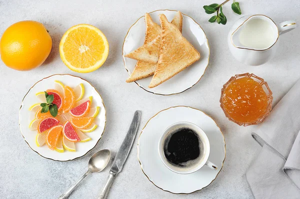 Coffee with toast. Toasts are served with orange jam. Marmalade and oranges complete the composition. The concept of a romantic breakfast. View from above. Light background.