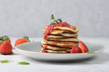 Çilek şuruplu krep. Çörekler taze çilek ve nane yapraklarıyla süslenir. Çilekler masanın yüzeyine saçılmış. Hafif arkaplan.