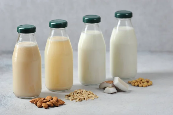 Concept alternative to cow\'s milk.  Bottles with coconut, oat, soy and almond milk.  Next to the bottles are pieces of coconut, almonds, oatmeal and soybeans.  Light background.  Close-up.