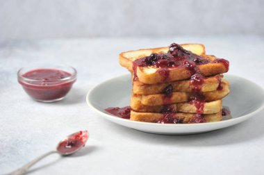 Tabakta çilek reçeli tost. Yanında reçel ve kaşık olan bir fincan. Hafif arkaplan. Yakın plan..