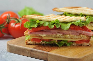 Ahşap tepside klasik kulüp sandviçi. Lezzetli sandviç dolgusu jambon, peynir, dilimlenmiş domates, marul ve sostan oluşur. Arka planda domates ve marul var. Yakın plan..