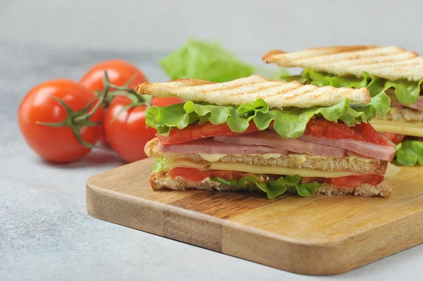经典的俱乐部三明治在木制托盘上 美味的三明治馅包括火腿 切碎的西红柿 生菜和酱汁 背景是西红柿和生菜 后续行动 — 图库照片