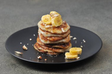 Siyah tabakta küçük gözlemeler. Krepler muz, fındık ve bal ile servis edilir. Yakın plan. Gri arkaplan.