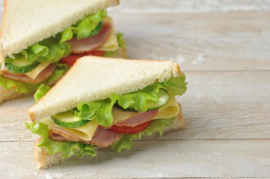 Beyaz ekmekten yapılmış jambonlu ve peynirli sandviç. Hafif ahşap zemin. Metin için boş alan.