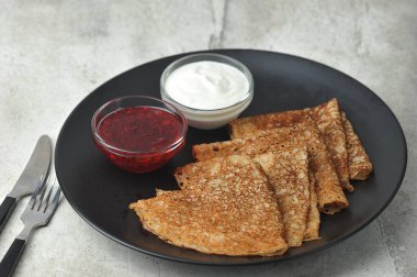 Siyah tabakta ince krepler. Kremalı bardaklar ve krep yanında reçel. Hafif arkaplan. Yakın plan..