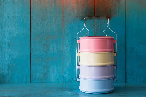 Mavi ahşap masada ve açık mavi arka plan duvarında renkli retro yemek taşıyıcısı olan.