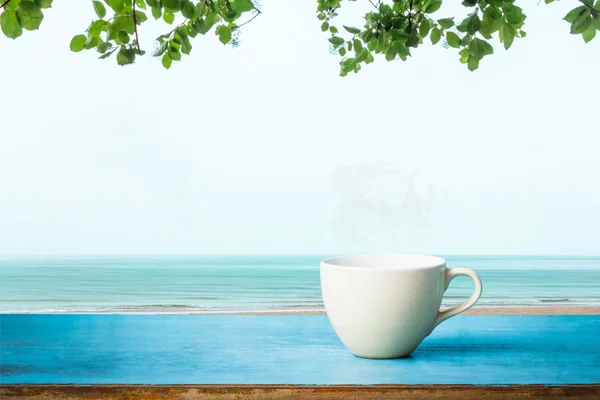 Eski ahşap masanın üzerinde füme fincanlı sıcak kahve, deniz sahili arka planında..